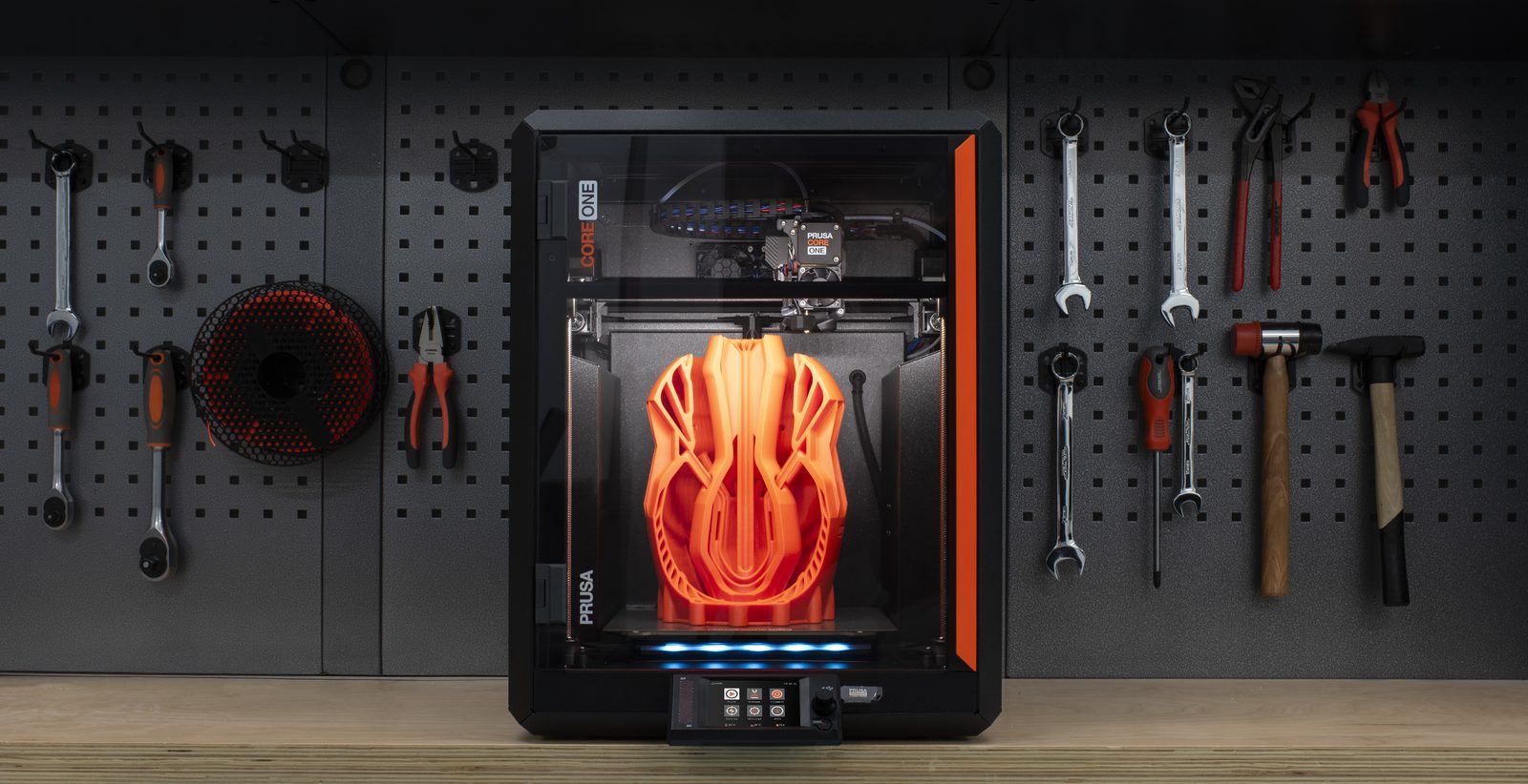 Prusa CORE One de primera generación en un taller, sobre un banco con herramientas colgadas detrás